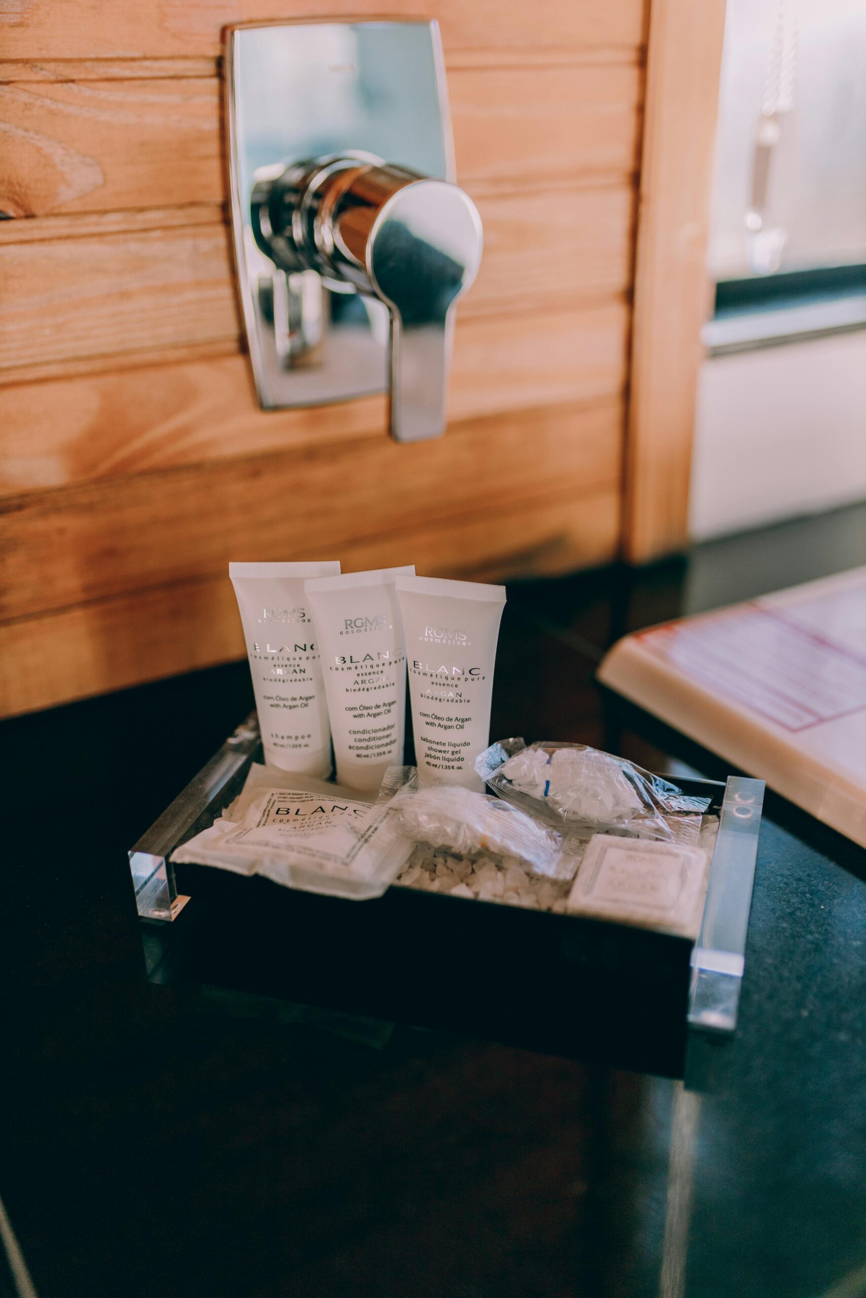 Elegant hotel bathroom amenities placed on a wooden counter beside a chrome faucet.